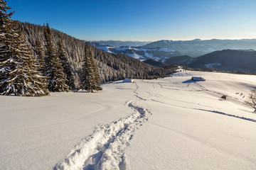 Winter Christmas landscape of mountain valley on frosty sunny day. Old wooden forsaken shepherd hut...