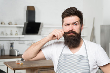 Fototapeta premium Curling his long moustache. Professional cook confident in his cooking skills. Bearded man during cooking in kitchen. Home-cooking and commercial cooking. The art of cooking