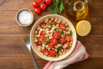 White bean salad with tomatoes, capers, garlic and parsley in bowl on wooden table. Top view.