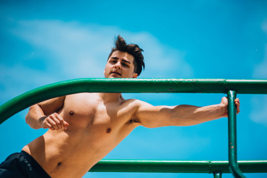 Physically fit man exercising outdoors doing triceps dips on parallel bars