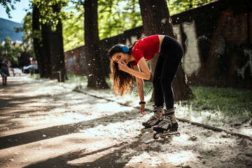 Woman lacing up rollers while standing in the park and listening music with headphones