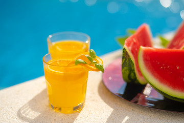 Summer holiday tropical concept. Fresh orange juice and watermelon juice and pineapple on border of a swimming pool.