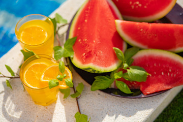 Summer holiday tropical concept. Fresh orange juice and watermelon juice and pineapple on border of a swimming pool.