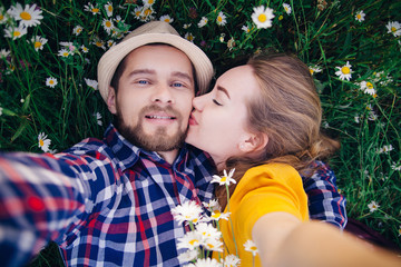 A girl in a bright yellow dress kisses a guy in a plaid shirt. They make selfie together