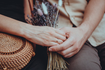 Bouquet of lavender flowers in girls hands. Engagement ring on hand. Love couple holding hands. Love, relationships, travel, romance concept.