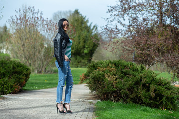 Brunette in sunglasses and black is standing and enjoying the sun in the park