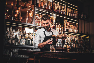 Fototapeta na wymiar Serious barman is prepairing drinks for customers at posh bar.