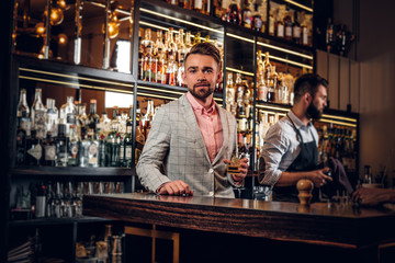 Obraz premium Przystojny, nowoczesny mężczyzna w kraciastym garniturze spożywa alkohol w modnym barze.