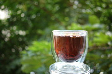 Black tea in clear glass cup on the nature on green blurred background.
