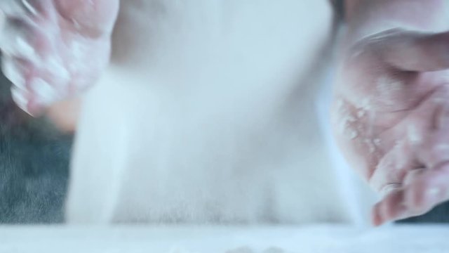 Young adult chef clapping his hands filled with flour. Concept: the production of sweets pies pastry dough, gourmet, pure product, baking, work in restaurants, bake beautiful products