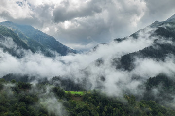 Georgian mountains cloudscape with small meadow seen from clouds