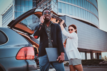 Cheerful sucessful business partners in sunglasses are meeteng up near big offices building.