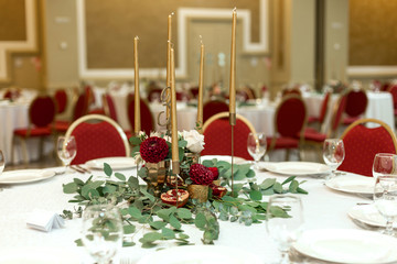 Festively decorated round banquet table in the restaurant. Fresh flowers are golden candles and red chairs. expensively rich