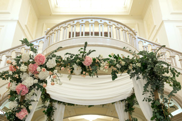 Fototapeta na wymiar Wedding chuppah decorated with fresh flowers indoor banquet hall of wedding ceremony. Luxury wedding florist decoration artwork
