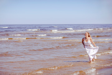 Fototapeta na wymiar Happy smiling woman in white dress running to the sea. Copy space