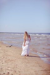 Fototapeta na wymiar Portrait from behind of young woman in white dress, walking to the water on the beach