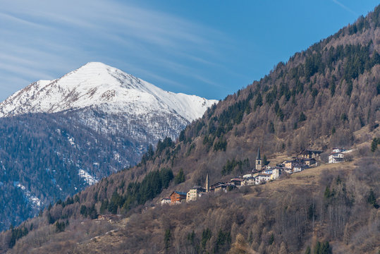 Spring in Italian Alps. The sun, cloudy sky and snow covered mountains. View on Termenago - small Italian village near Ski region Val di Sole, Alps, Trento, Italy, Europe