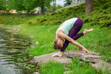 Thin brunette girl plays sports and performs beautiful and sophisticated yoga poses in a summer...