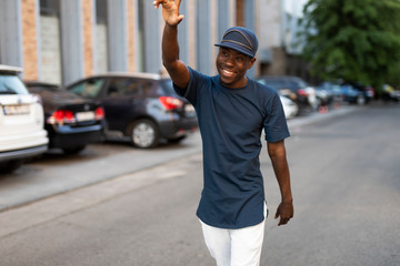 Happy african american man greets a friend waving his hand walking in city street, he glad to see you