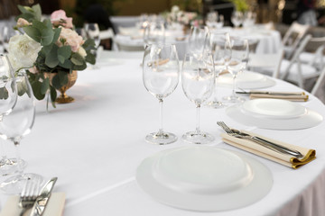 Wedding table setting decorated with fresh flowers in a brass vase. Wedding floristry. Banquet table for guests outdoors with a view of green nature. Bouquet with roses, eustoma and eucalyptus leaves