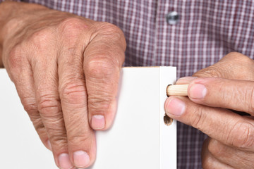 Closeup of a man assembling a DIY piece of furniture. The worker is inserting a wooden dowel into a pre-drilled hole