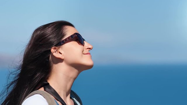 Close-up face of pleasant woman traveler in sunglasses playing with hair at sea sky background