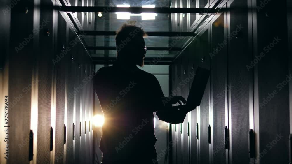 Poster silhouette of a man working on a laptop in a server room. datacenter server room concept.