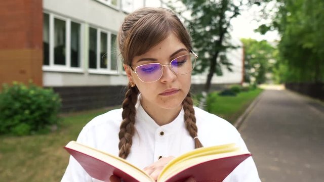 Serious  young girl in glasses reading book near school, university, motivated student with big dreams studying abroad, creative happy manager starts successful career