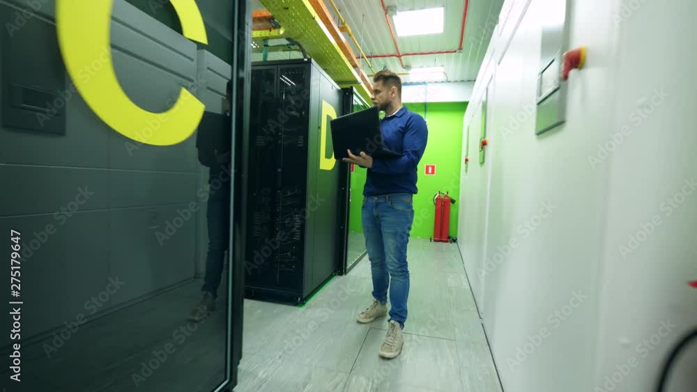 Poster a man with a laptop is observing a room with server blocks
