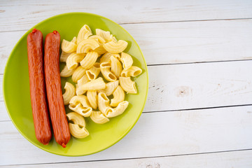 pasta and sausages in a green plate on a wooden table. pasta in closeup