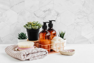 Soap and shampoo bottles and cotton towels with green plant on white table inside a bathroom background.