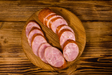 Cutting board with sliced sausage on a wooden table. Top view