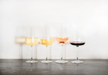Variety of wine types. Light and full-bodied white, rose and red wine in glasses in row over concrete table, white wall background, copy space. Wine list for cafe, wine boutique or degustation