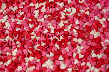 Fototapeta na wymiar Small candy in the shape of a heart is scattered over the background. Many small bright hearts in bulk. Pink, red and white candy.