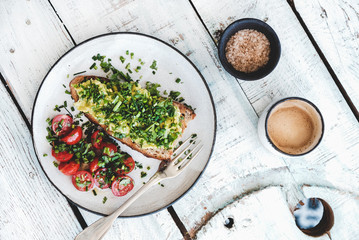 Healthy vegan lunch. Flat-lay of avocado toast on sourdough bread with chives, coriander, cherry-tomatoes with cup of coffee over white background, top view. Vegetarian, clean eating concept