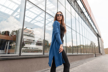 Stylish young hipster woman in a blue knitted long cape in a top in jeans in a sunglasses walks...