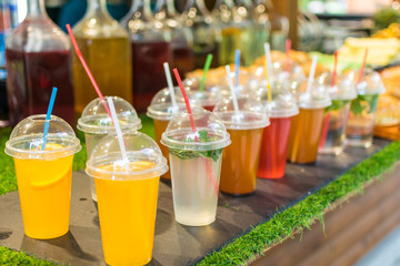 Many different colorful cocktails in plastic cups with tubes.