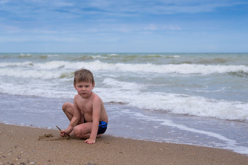 A little boy plays near the water by the sea.