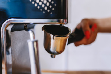 Barista holds portafilter with coffee for making espresso. Female hand holds metal portafilter with ground coffee and attaches it to the coffee machine. Concept making coffee. Toned picture
