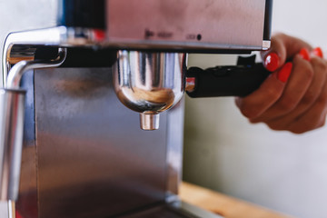 Barista holds portafilter with coffee for making espresso. Female hand holds metal portafilter with ground coffee and attaches it to the coffee machine. Concept making coffee. Toned picture
