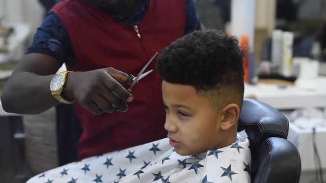Boy in the african barbershop. Cute mixed boy makes a haircut in the African salon. Hair style. Haircut by machine for children. School boy hair style. Haircut by scissor