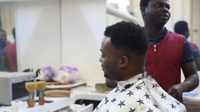 Black man in the african barbershop. Cute black man makes a haircut in the African salon. Hair style. Haircut by machine for adults. Shaving with barber.