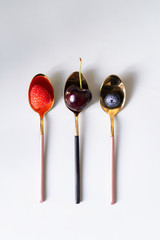 On teaspoons of black and pink color are summer berries raspberries, blueberries and cherries. New luxury Golden cutlery view from above on a isolated white background. Top view.