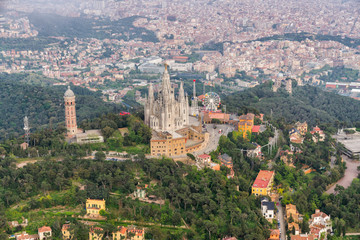 Flying around Tibidabo mountain with amusement park overlooking city of Barcelona, Spain. Aerial helicopter view