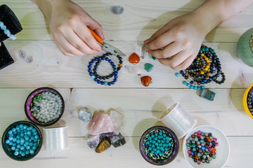 High angle view of Young woman making crystal jewelery necklace and bracelet at home manually