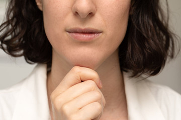 An extreme closeup view of a young Caucasian woman squeezing the layer of fat beneath the jawline, commonly called a double chin, body dysmorphia concept.