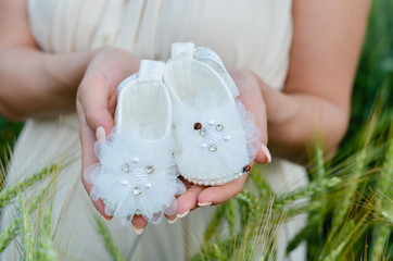 Young caucasian pregnant women hands  holding baby girl shoes in anticipation of the child.