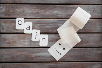 Toilet paper roll with painted face and pain copy for proctology diseases concept on wooden...