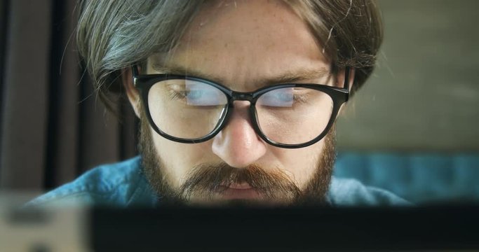 Concentrated young man in eyeglasses working on tablet, freelancer searching project, reflection
