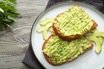 Plate with tasty avocado toasts on wooden table